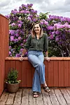 Person sitter på ett altanräcke framför en tät vägg av lila rhododendron.
