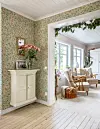 Ljust vardagsrum i trähus med blommig tapet, vita möbler och stora fönster.