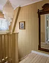 Trapphall med brädväggar, kristallampa, tavla och stor snidad spegel.