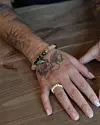 Tatuerad hand med pärlring och armband liggande på ett träbord.