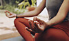 Närbild på händer i mudra under meditation i korslagd sittställning utomhus.