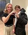 Två personer står inomhus och formar ett hjärta med sina händer.