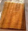 Gammal brun läderbunden bok med texten Mors minne på ett dukat bord i varmt solljus.