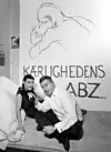 Ett par sitter på golvet framför en vägg med texten ”Kærlighedens ABZ” och en tecknad omfamning.