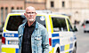 Äldre man i jeansjacka står framför svensk polisbil på stadsgata.