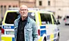 Äldre man i jeansjacka står framför svensk polisbil på stadsgata.