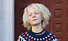 Ung blond person i mönstrad tröja framför en rödbrun trädörr.