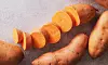 Skivad sötpotatis omgiven av hela sötpotatisar på ljus yta.
