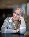 Carina Bergfeldt lutar huvudet mot handen vid ett bord inomhus.