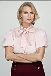 Sanne Gottlieb i lys pink bluse og mørke bukser står med korslagte arme mod lys baggrund.
