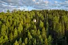 Litet trähus högt uppe bland täta gröna tallar i ett stort skogsområde.