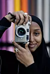 Närbild på fotograf som håller en kamera framför ansiktet mot färgglad bakgrund.