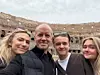 Fyra personer tar en selfie framför Colosseum i molnigt dagsljus.