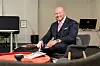Dennis Lavesson i kostym sitter i kontorslounge med rött bord. Man skymtar datorer bakom honom.