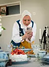 Kvinna i Sverigedräkt och hijab fotograferar ett dukat bord med midsommarmat.
