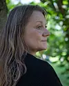 Kvinna i profil utomhus framför suddig grönska och träd