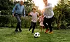 Vuxna och barn springer efter en fotboll på en gräsmatta i trädgården.