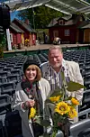 Två skådespelare står med solrosbukett bland tomma stolsrader framför en friluftsteater.
