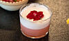 Ett lågt glas med rosa drink och vitt skum, dekorerad med ett rött blomblad på toppen.