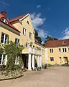 Gul byggnad med röda tak, vit entré och grusgård under blå himmel.