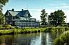 Ett stort hotell med glasveranda står vid vattnet omgiven av grönska.