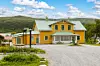 Gult hotell med grön takplåt, grusparkering och fjäll i bakgrunden.