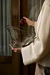 En person i ljus klädsel håller en stor genomskinlig glasskål med båda händerna.