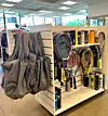 Hylla med tennisracketar, bollar och sportartiklar i en ljus butikslokal med gråa plagg hängande i förgrunden.