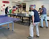 Personer spelar bordtennis i en ljus lokal med hyllor fyllda av sportutrustning.
