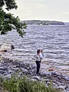 En person står på en stenig strand vid en sjö med vågigt vatten och trädbevuxna öar i fjärran.
