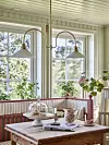 Glasveranda med randig soffhörna, träbord, växter och stora fönster mot trädgården.