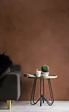 Minimalistiskt rum med brun vägg, grå soffa, runt sidobord och en liten kaktus i kruka.