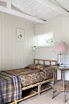 Liten sovdel med träpanel, enkelsäng, nattduksbord, rutig lampskärm och ett litet fönster.