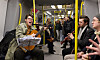 En musiker med gitarr uppträder i en tunnelbanevagn medan resenärer sitter och lyssnar.