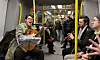 En musiker med gitarr uppträder i en tunnelbanevagn medan resenärer sitter och lyssnar.