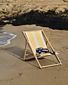 En träsolstol med gulvita ränder står på sand nära vattenlinjen.