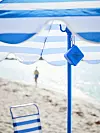 Blåvit parasoll och en randig strandstol på sandig strand med hav i bakgrunden.