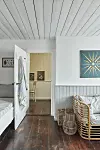 Ljust rum med vita panelväggar, mörkt trägolv, flätad soffa, korgar och blå väggkonst.