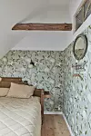 Litet sovrum med träbädd, beige sängkläder, blommig tapet och rund väggspegel.