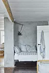 Smal sovhörna med säng, betongvägg, vit dörr och blåvit textil i ett ljust rum.