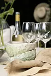 Uppdukad utomhusbord med vinflaska, tre vinglas, två keramiska skålar, skedar och beige servetter.