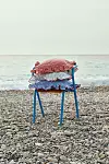 Ett blått bord med röd- och blårutiga textilier står på en stenstrand framför havet.