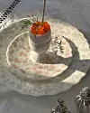 Två mönstrade porslinstallrikar med ett glas och en blomsterdekoration på en vit duk i solljus.