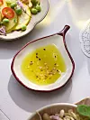 En vit och röd keramikskål med gul dressing står på ett dukat bord med flera assietter runtom.