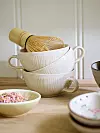 Två staplade ljusa skålar med matcha-visp på ett träbord, omgivna av små assietter.