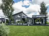 Modern svart villa med trädgård, gräsmatta, krukor och uterum under blå himmel.