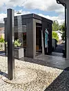 Mörkt uterum med glasade partier, trädäck, grus och en klädhängare vid en modern trädgård.