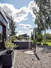 Grusbelagd trädgård med jacuzzi, planteringskärl, träd och ett modernt hus i kanten av bilden.