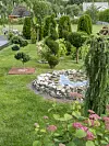 Trädgård med flera formklippta buskar, grusgång, blommor och en liten stenlagd damm.