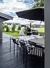 Altan med dukat bord, stor grill och parasoller, med gräsmatta, träd och hus i bakgrunden.
